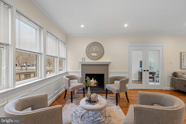 sitting room with a decorative wall, wood finished floors, french doors, a brick fireplace, and crown molding