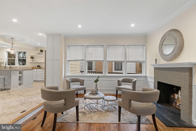 living area with a brick fireplace, ornamental molding, light wood-style floors, and recessed lighting