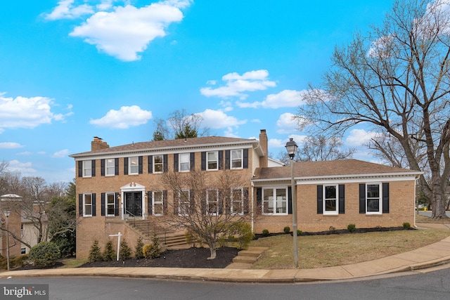 colonial house featuring brick siding, a chimney, and a front yard