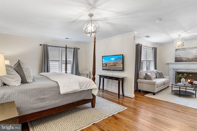 bedroom featuring ornamental molding, an inviting chandelier, a premium fireplace, and wood finished floors