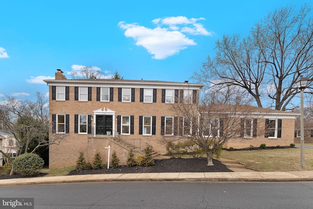 view of front facade featuring brick siding, a chimney, and a front yard