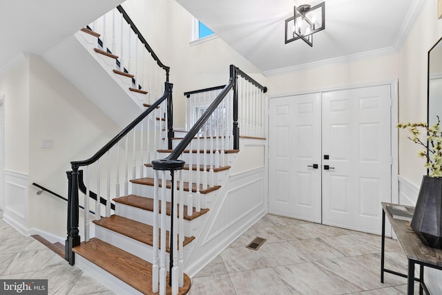 foyer entrance featuring a decorative wall, crown molding, visible vents, stairs, and an inviting chandelier