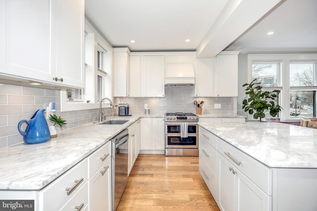 kitchen featuring stainless steel appliances, white cabinetry, a sink, and premium range hood