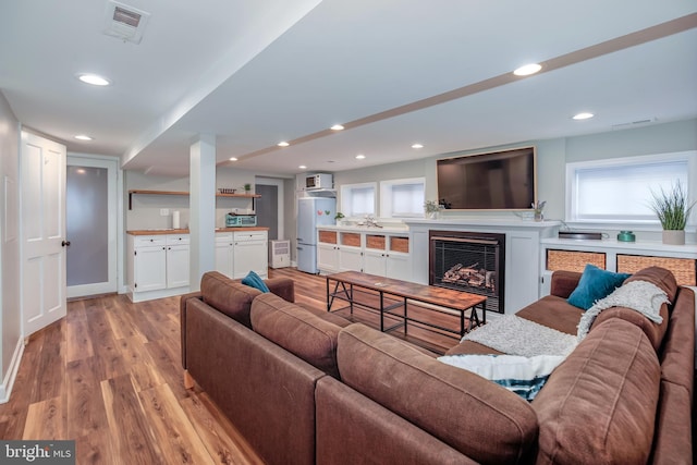 living room featuring light wood-type flooring, a fireplace, visible vents, and recessed lighting