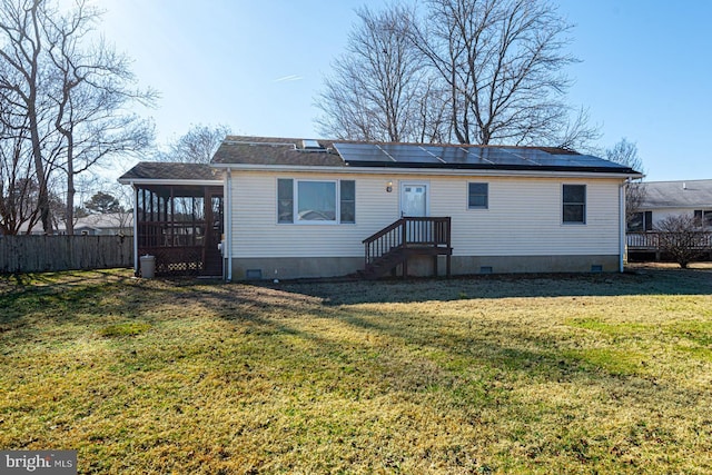 rear view of property featuring a yard, crawl space, a sunroom, and roof mounted solar panels