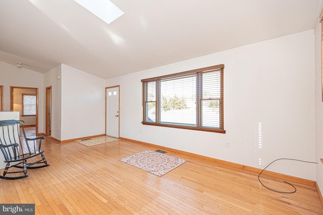 interior space featuring lofted ceiling with skylight, wood finished floors, visible vents, and baseboards