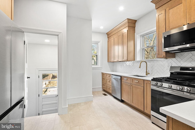 kitchen with a sink, a healthy amount of sunlight, light countertops, appliances with stainless steel finishes, and tasteful backsplash