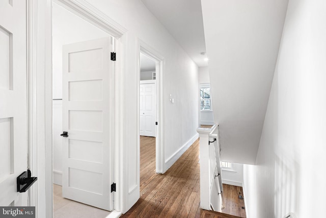 hall with wood finished floors, an upstairs landing, and baseboards