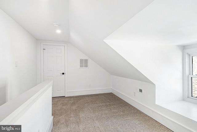 additional living space with light carpet, baseboards, visible vents, and lofted ceiling