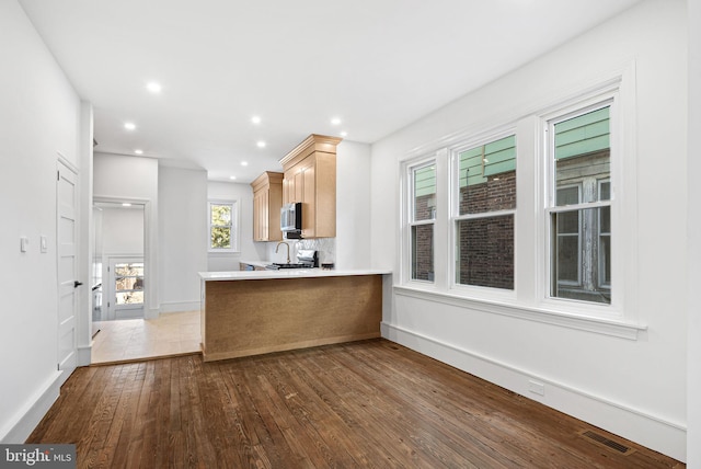 kitchen featuring visible vents, dark wood-style floors, stainless steel microwave, a peninsula, and light brown cabinets