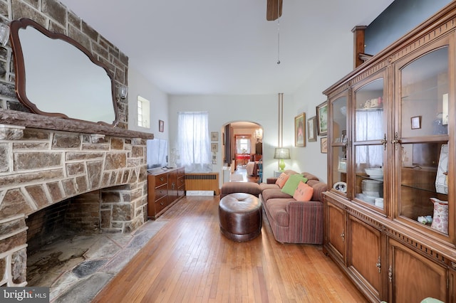 living area featuring light wood-type flooring, radiator heating unit, a fireplace, and arched walkways