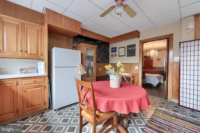 dining area with a ceiling fan, a wainscoted wall, wooden walls, and a drop ceiling