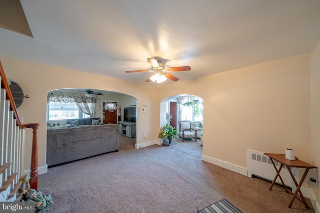 unfurnished living room with baseboards, stairs, carpet flooring, arched walkways, and a ceiling fan