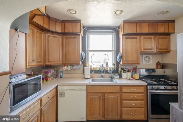 kitchen featuring light countertops, recessed lighting, appliances with stainless steel finishes, brown cabinetry, and a sink