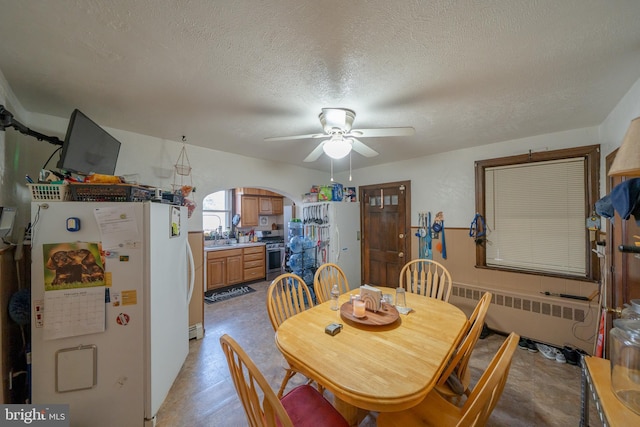 dining room with radiator heating unit, a ceiling fan, arched walkways, and a textured ceiling