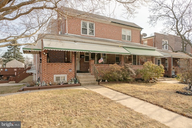 view of front of property featuring a front lawn, covered porch, and brick siding