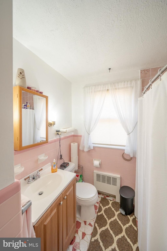 full bath featuring toilet, a textured ceiling, radiator, tile walls, and vanity