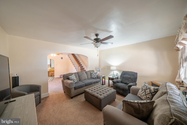 living area featuring a ceiling fan, baseboards, arched walkways, stairs, and light colored carpet