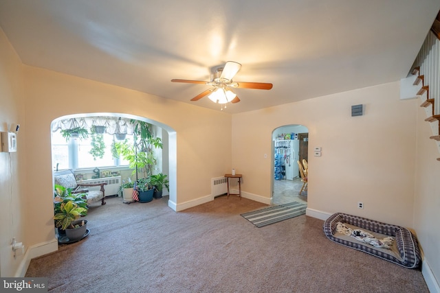 living area featuring radiator, baseboards, arched walkways, ceiling fan, and carpet flooring