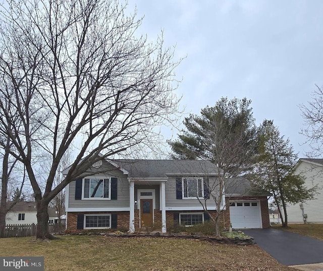 split foyer home featuring aphalt driveway, a garage, brick siding, fence, and a front lawn