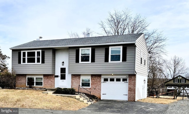 raised ranch with driveway, brick siding, an attached garage, and a shingled roof