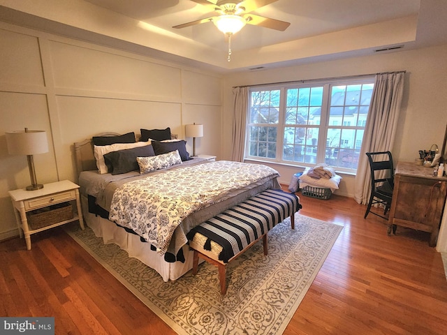 bedroom with wood finished floors, a raised ceiling, visible vents, and a decorative wall