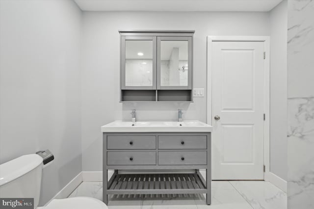 bathroom with marble finish floor, double vanity, toilet, and baseboards