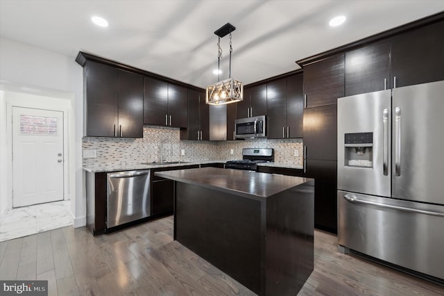 kitchen featuring a center island, stainless steel appliances, hanging light fixtures, a sink, and wood finished floors