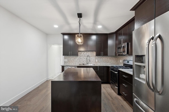 kitchen with dark brown cabinetry, stainless steel appliances, a sink, a kitchen island, and pendant lighting