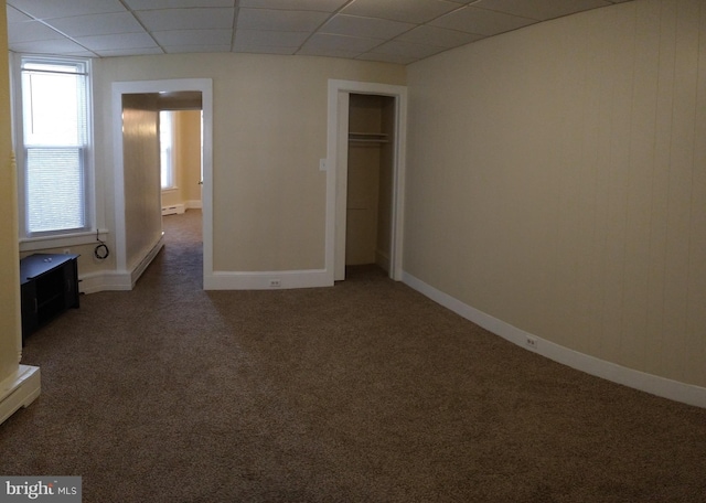 unfurnished bedroom featuring a baseboard heating unit, dark colored carpet, a closet, and a paneled ceiling