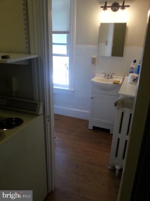 bathroom featuring tile walls, radiator heating unit, wainscoting, vanity, and wood finished floors