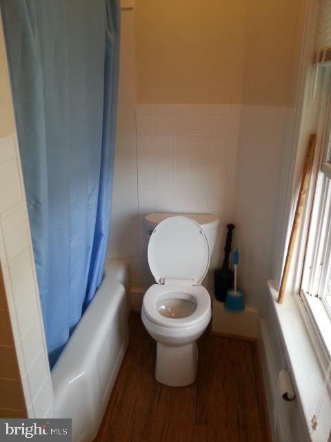 full bathroom with shower / tub combo, wainscoting, toilet, wood finished floors, and tile walls