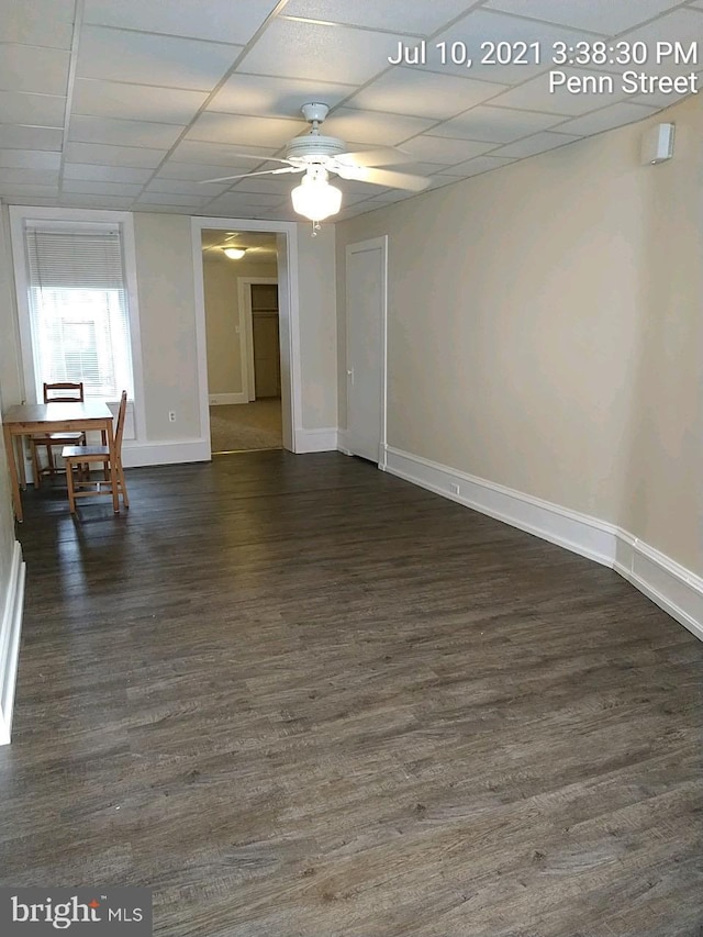 unfurnished room featuring ceiling fan, baseboards, a drop ceiling, and dark wood-type flooring