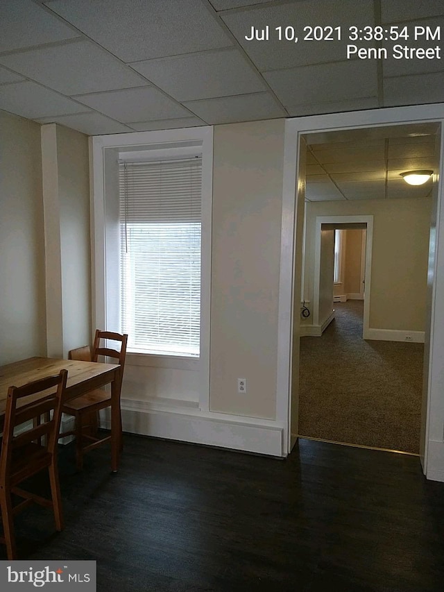 unfurnished dining area featuring dark wood-style floors, a drop ceiling, and baseboards