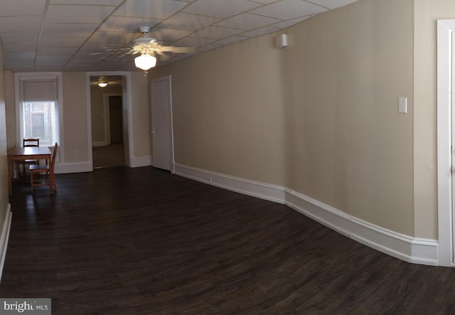 unfurnished room featuring dark wood-style floors, ceiling fan, a drop ceiling, and baseboards