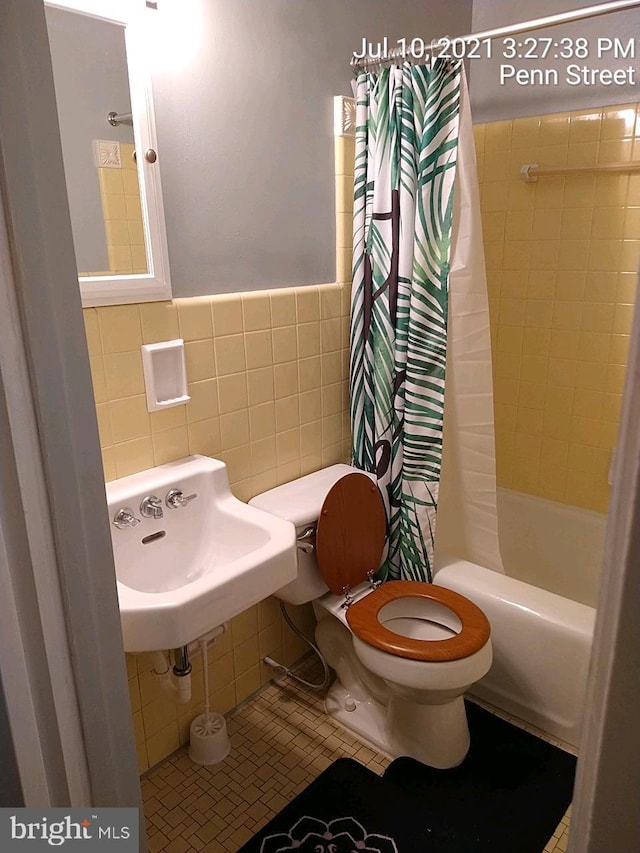 bathroom with tile walls, toilet, tile patterned flooring, shower / bath combo with shower curtain, and a sink