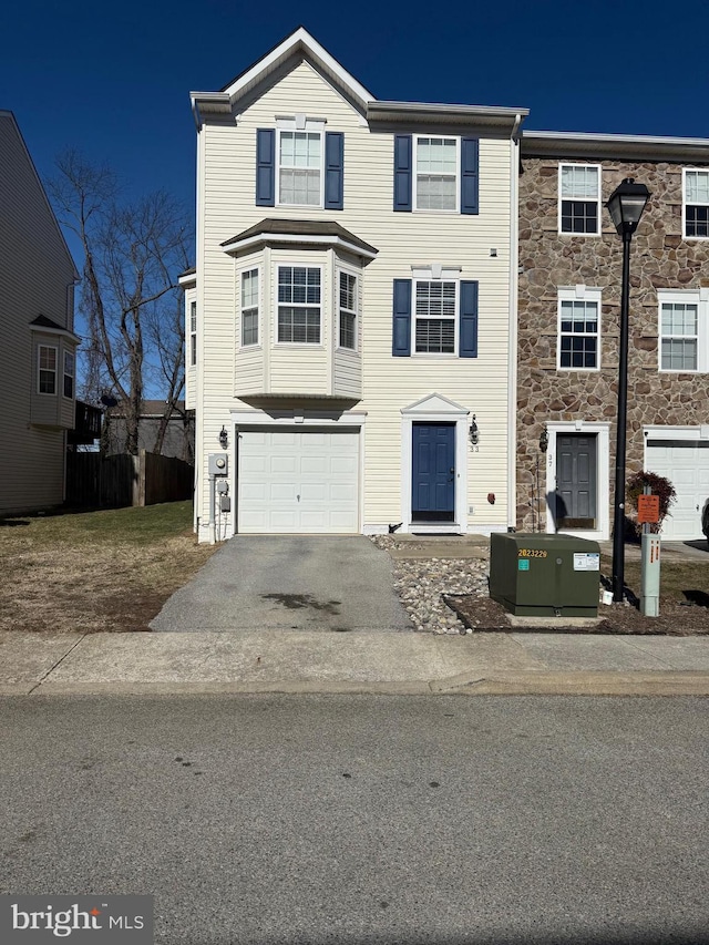 multi unit property featuring an attached garage, stone siding, and driveway