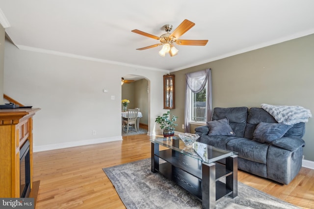 living room featuring baseboards, arched walkways, ceiling fan, crown molding, and light wood-style floors