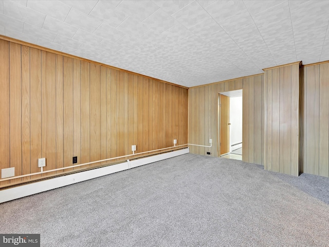 carpeted spare room featuring wood walls and baseboard heating