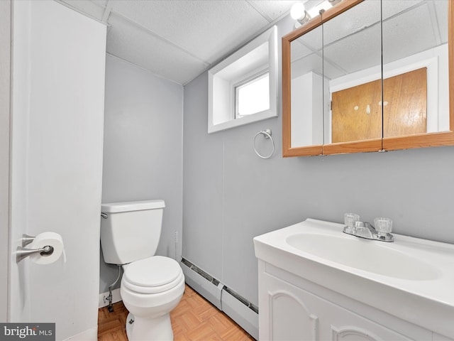 half bathroom featuring a baseboard heating unit, toilet, and vanity