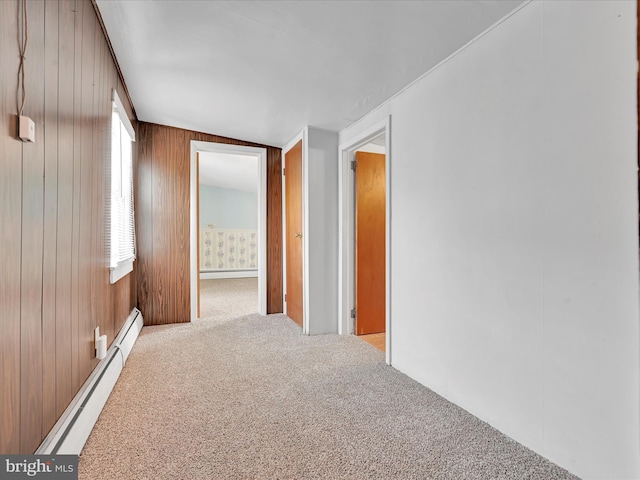 hallway featuring wood walls, a baseboard heating unit, baseboard heating, and light colored carpet