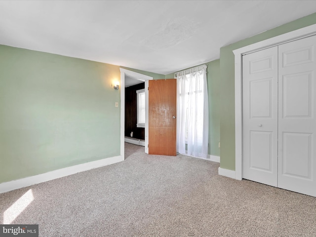 unfurnished bedroom featuring a baseboard heating unit, a closet, baseboards, and light colored carpet