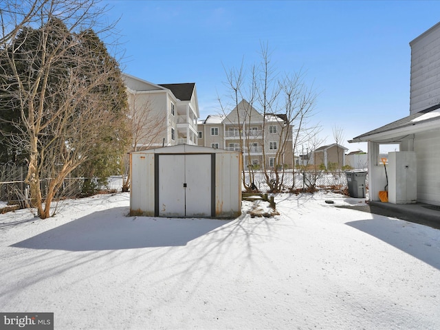 snowy yard featuring an outbuilding, fence, a residential view, and a shed