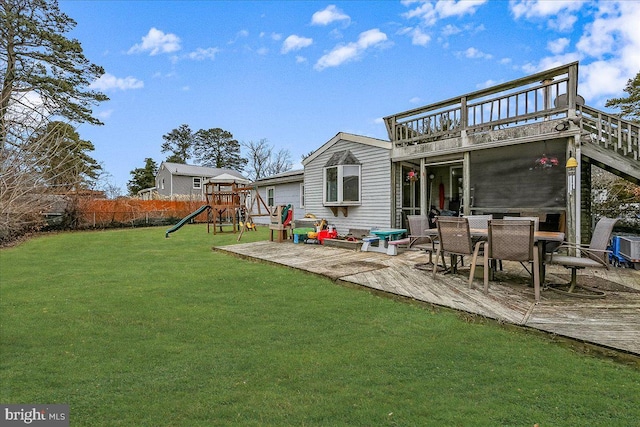 rear view of property featuring a lawn, fence, outdoor dining area, a deck, and a playground