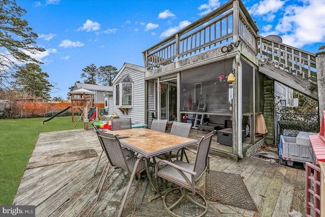 wooden terrace with a yard, outdoor dining area, a playground, and fence