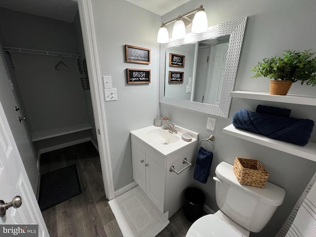 bathroom with a spacious closet, toilet, vanity, wood finished floors, and baseboards