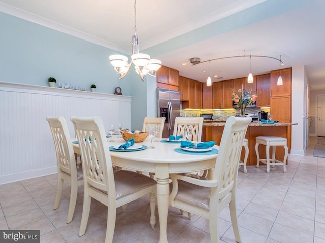 dining space with an inviting chandelier, light tile patterned floors, ornamental molding, and wainscoting