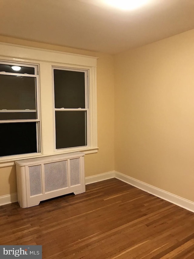 empty room with radiator heating unit, dark wood finished floors, and baseboards