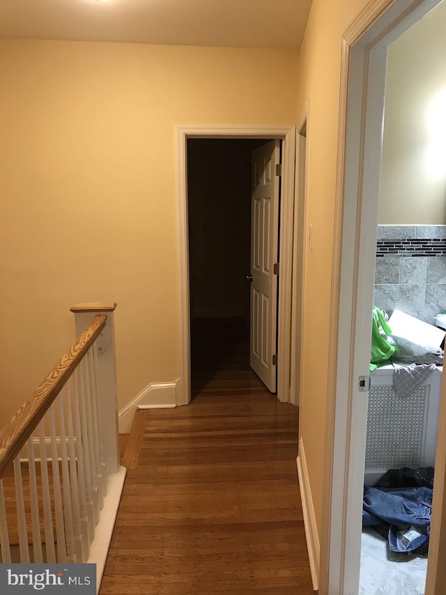 hall with wood finished floors, an upstairs landing, and tile walls