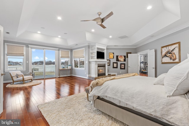 bedroom with baseboards, access to outside, a tray ceiling, wood-type flooring, and a glass covered fireplace